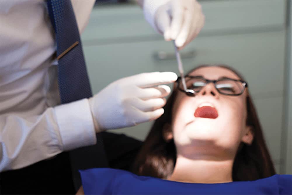 young woman is in a dental chair while a doctor examining her teeth