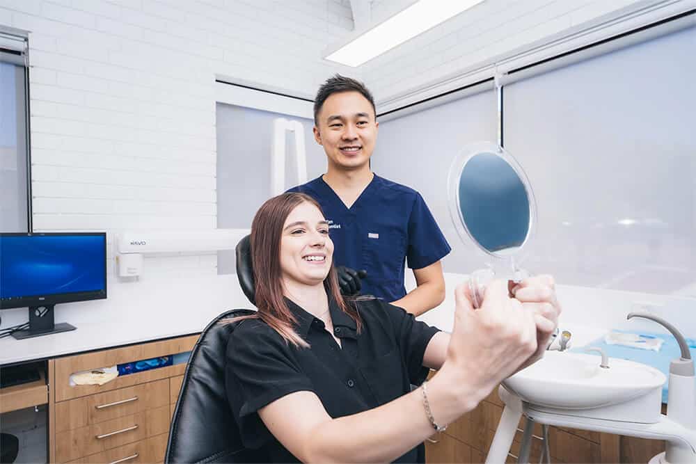 Happy patient of Dr.Kent Tan is looking at her new smile in the mirror